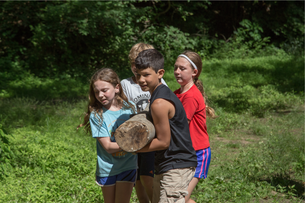 Children carrying a log together outdoors.